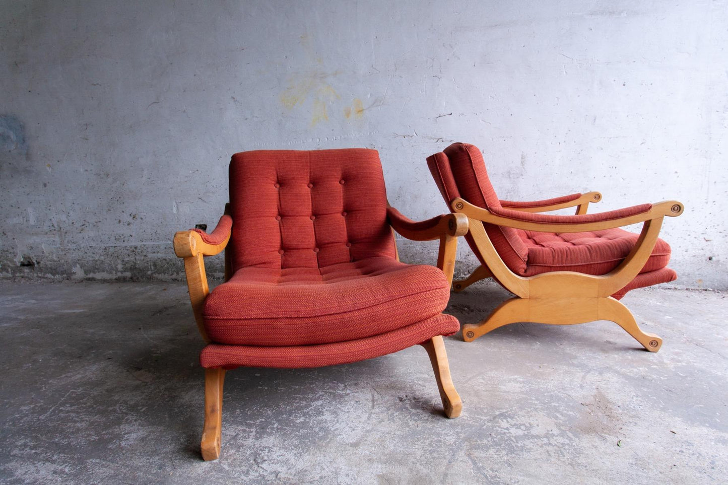 Pair of red fabric and wooden club chairs with soft lined design.